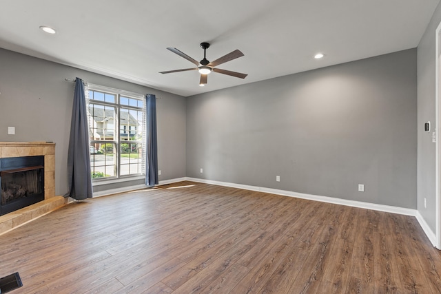 unfurnished living room featuring a ceiling fan, a fireplace with raised hearth, wood finished floors, baseboards, and recessed lighting