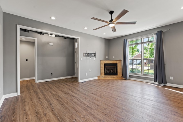 unfurnished living room with a ceiling fan, wood finished floors, a tiled fireplace, baseboards, and recessed lighting