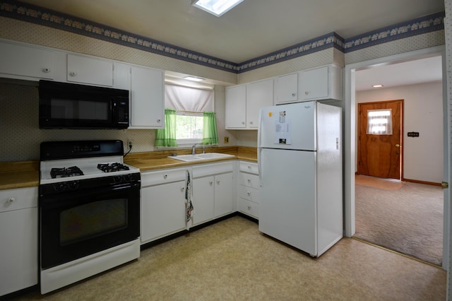 kitchen with black microwave, freestanding refrigerator, range with gas stovetop, a sink, and white cabinets