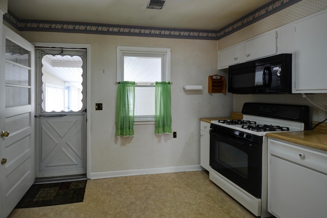 kitchen featuring black microwave, gas stove, light flooring, white cabinets, and baseboards