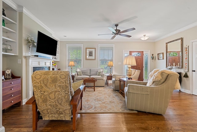 living area with wood finished floors, ceiling fan, ornamental molding, a fireplace, and baseboards