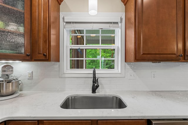 kitchen featuring a sink, tasteful backsplash, dishwasher, light stone countertops, and glass insert cabinets