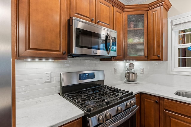 kitchen with appliances with stainless steel finishes, backsplash, glass insert cabinets, and brown cabinets