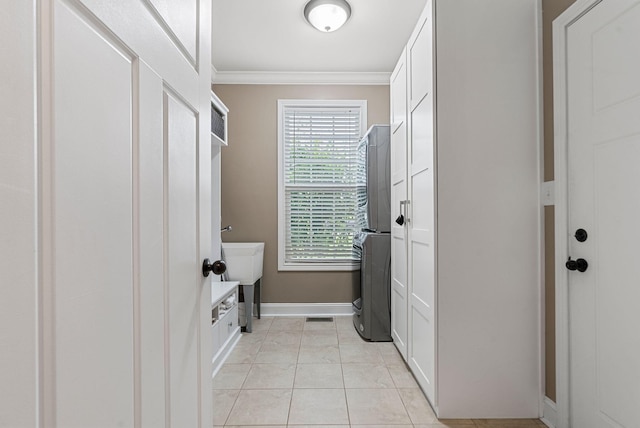 mudroom featuring ornamental molding, stacked washer and clothes dryer, light tile patterned floors, baseboards, and a sink