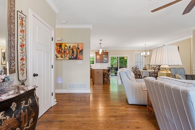 living area featuring ceiling fan, wood finished floors, ornamental molding, a chandelier, and baseboards