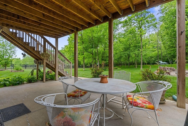 view of patio featuring stairs, view of wooded area, and outdoor dining space