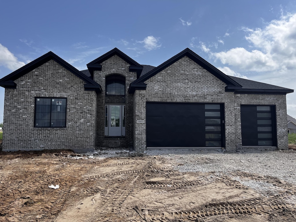 french provincial home with brick siding, an attached garage, and dirt driveway