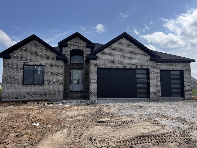 french provincial home with brick siding, an attached garage, and dirt driveway