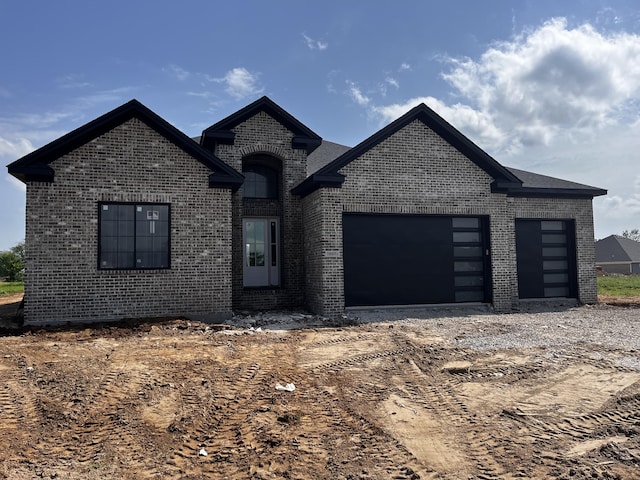 french country style house with brick siding, a garage, and driveway