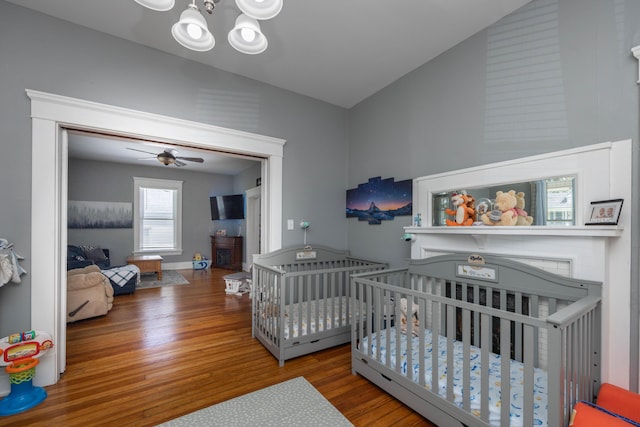 bedroom with vaulted ceiling, wood finished floors, a chandelier, and a nursery area