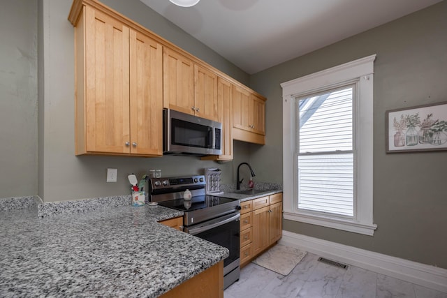 kitchen featuring appliances with stainless steel finishes, light marble finish floors, light stone counters, and baseboards
