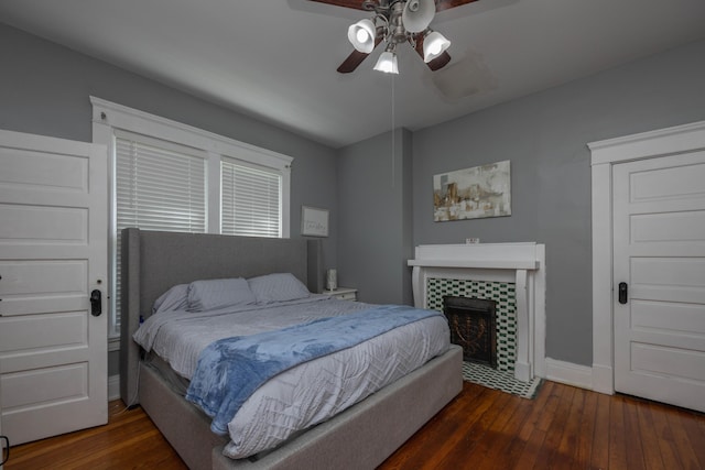 bedroom with wood-type flooring, baseboards, a tiled fireplace, and ceiling fan