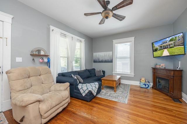 living area featuring light wood-type flooring, ceiling fan, a glass covered fireplace, and baseboards