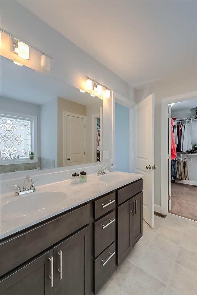 full bath with double vanity, a spacious closet, and tile patterned flooring