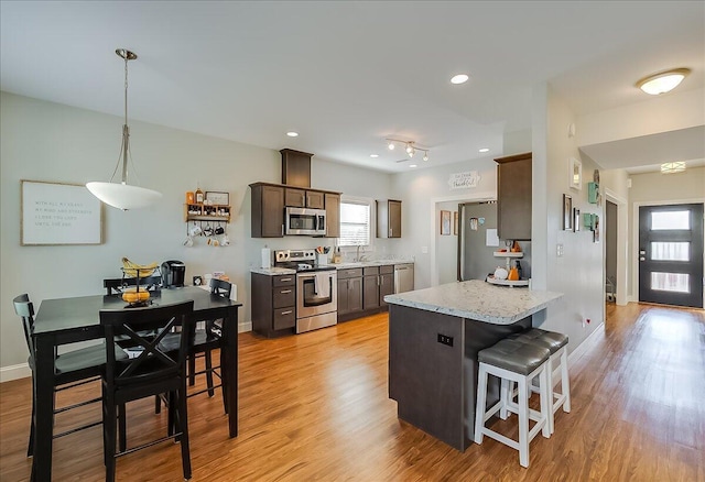 kitchen with stainless steel appliances, dark brown cabinets, a breakfast bar, and light wood-style flooring