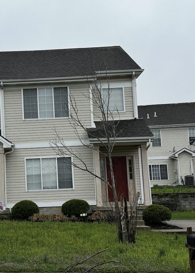 traditional-style house featuring a front lawn, central air condition unit, and a shingled roof