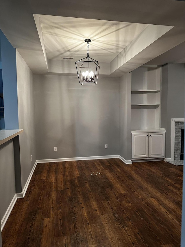 unfurnished dining area featuring dark wood-style floors, baseboards, a chandelier, built in shelves, and a fireplace with flush hearth
