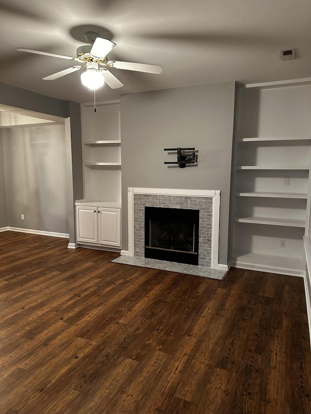 unfurnished living room with ceiling fan, a fireplace, dark wood finished floors, built in shelves, and baseboards