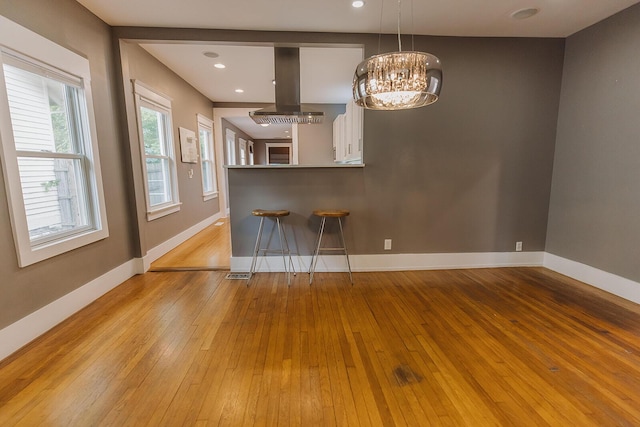 1010 Aurora Ave, Lexington, KY 40502 - kitchen with range hood, light wood-style floors, a breakfast bar, a chandelier, and baseboards