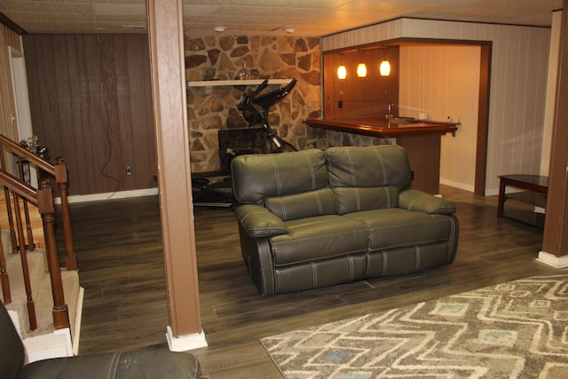 living room featuring baseboards, wood finished floors, stairway, wooden walls, and bar with sink