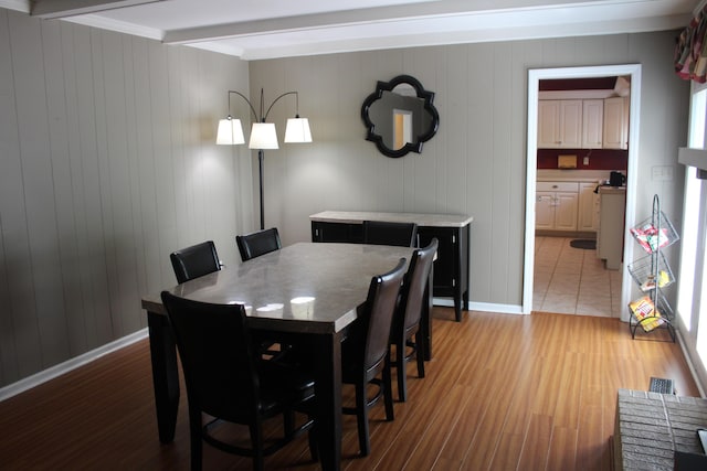 dining space featuring beam ceiling, light wood-style floors, baseboards, crown molding, and wood walls