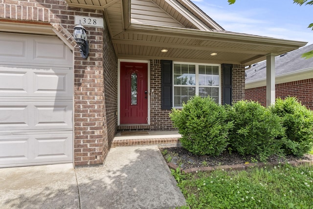 view of exterior entry featuring brick siding, a garage, and a porch