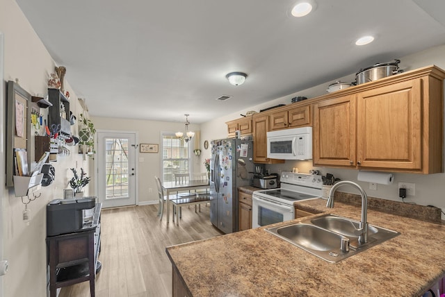 kitchen with white appliances, a sink, light wood finished floors, a chandelier, and brown cabinetry