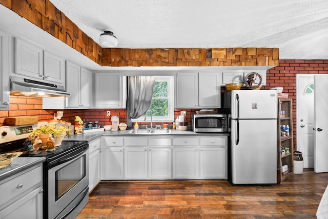kitchen featuring appliances with stainless steel finishes, under cabinet range hood, a sink, a textured ceiling, and backsplash