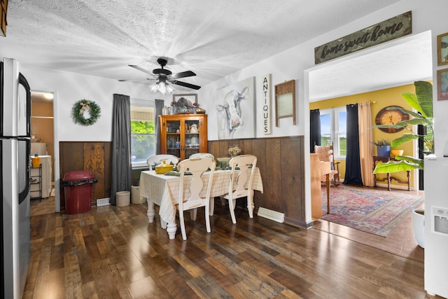 dining room with wainscoting, wood finished floors, a ceiling fan, a textured ceiling, and wooden walls