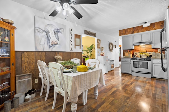 dining area with a ceiling fan, dark wood-style floors, wood walls, a textured ceiling, and wainscoting