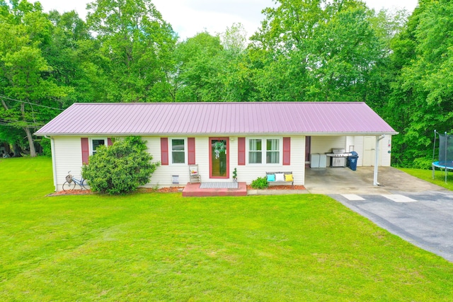 single story home featuring a trampoline, asphalt driveway, an attached carport, metal roof, and a front lawn