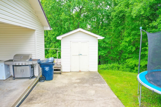 view of patio with a trampoline, grilling area, a storage unit, and an outdoor structure