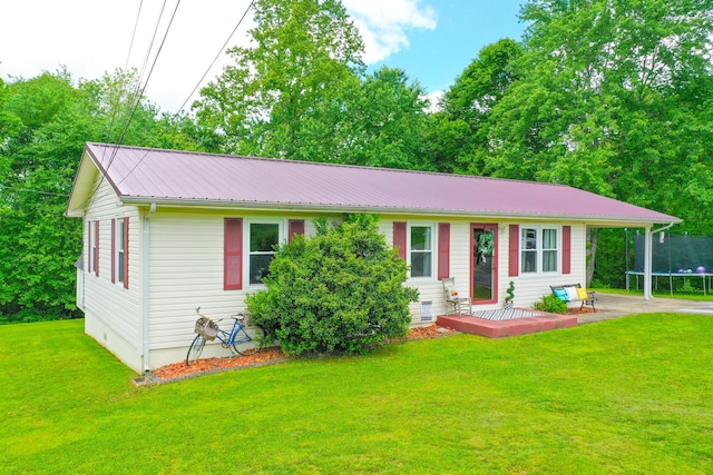 single story home with a trampoline, metal roof, a front lawn, and an attached carport