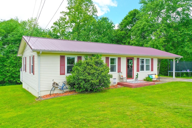 ranch-style home with a trampoline, metal roof, an attached carport, a front lawn, and a wooden deck