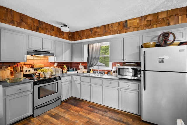 kitchen with appliances with stainless steel finishes, a sink, under cabinet range hood, a textured ceiling, and tasteful backsplash