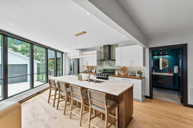 252 Cochran Rd, Lexington, KY 40502 - kitchen with wall chimney range hood, a sink, stainless steel appliances, light wood finished floors, and white cabinetry