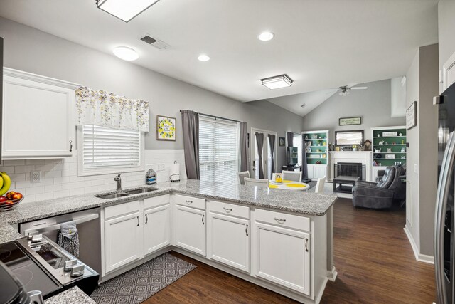 kitchen with a sink, a peninsula, a fireplace, ceiling fan, and white cabinetry