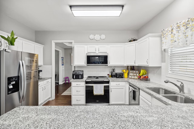 kitchen with stainless steel appliances, a sink, decorative backsplash, white cabinets, and light stone countertops