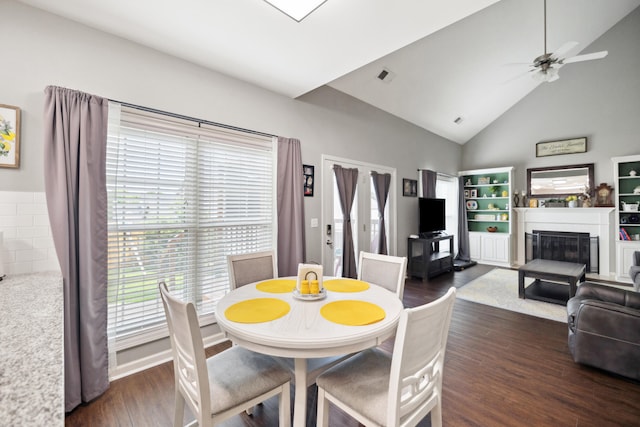 dining area featuring dark wood finished floors, a glass covered fireplace, high vaulted ceiling, and a ceiling fan