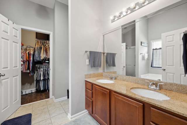 bathroom featuring a walk in closet, a garden tub, double vanity, and baseboards