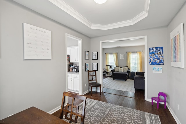 corridor featuring dark wood-style floors, a tray ceiling, baseboards, and ornamental molding