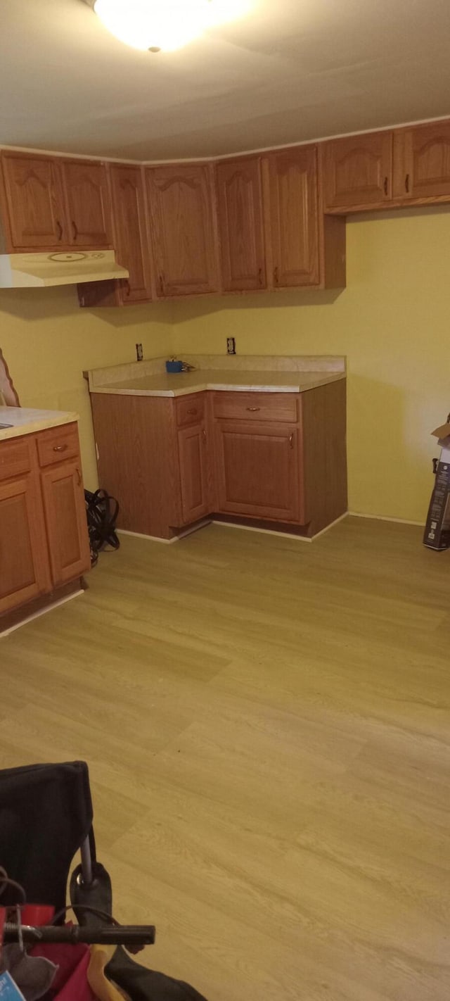 107 E N St, Carlisle, KY 40311 - kitchen with under cabinet range hood, brown cabinets, light countertops, and light wood-style flooring