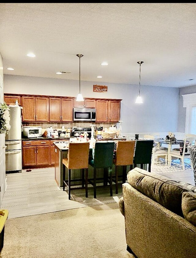 133 Mcintosh Park, Georgetown, KY 40324 - kitchen with stainless steel appliances, backsplash, hanging light fixtures, brown cabinets, and a kitchen breakfast bar