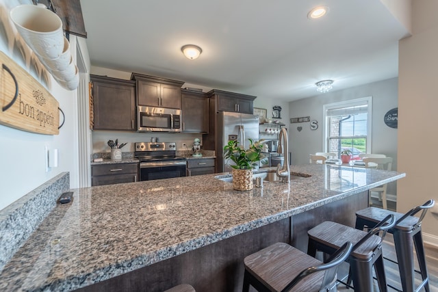 140 Central Park Ave, Berea, KY 40403 - kitchen with appliances with stainless steel finishes, a sink, a breakfast bar, dark brown cabinets, and dark stone counters