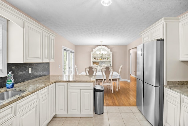 15 April Ln, Corbin, KY 40701 - kitchen featuring freestanding refrigerator, light tile patterned floors, a peninsula, a chandelier, and white cabinets