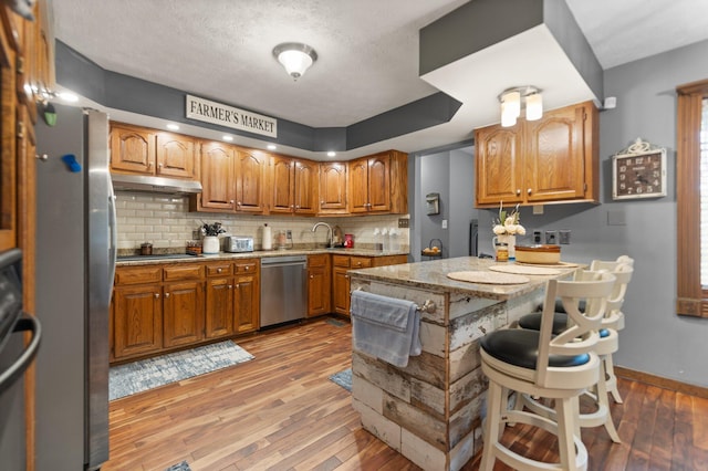 2003 Cresent Cir, Corbin, KY 40701 - kitchen featuring stainless steel dishwasher, under cabinet range hood, light wood finished floors, backsplash, and brown cabinetry