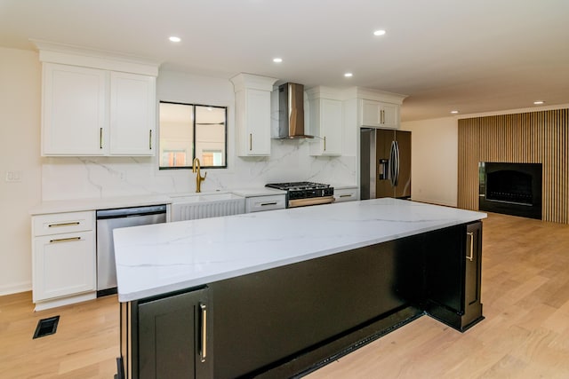 2933 Montavesta Rd, Lexington, KY 40502 - kitchen featuring appliances with stainless steel finishes, wall chimney range hood, a sink, light wood-style flooring, and white cabinetry