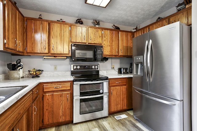 400 Aspen Dr, Lawrenceburg, KY 40342 - kitchen featuring stainless steel appliances, brown cabinets, light countertops, a textured ceiling, and light wood-type flooring