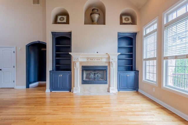 2433 San Milano Pl, Lexington, KY 40509 - unfurnished living room featuring light wood-style flooring, built in shelves, a fireplace, baseboards, and a high ceiling