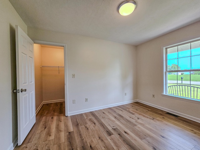 186 Amber Ln, Hustonville, KY 40437 - unfurnished bedroom featuring light wood-style flooring, a walk in closet, baseboards, a closet, and a textured ceiling